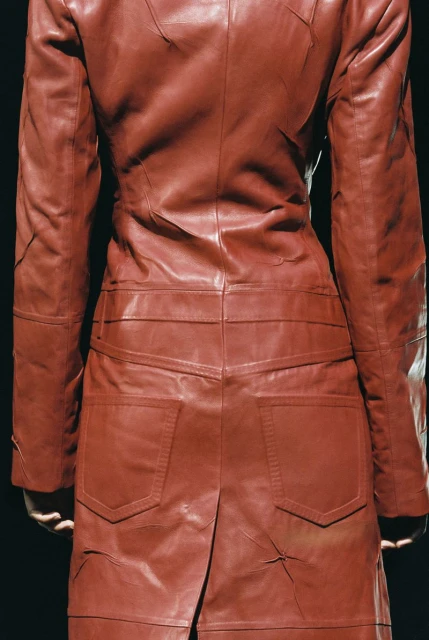 Rear view of a person wearing a red leather patchwork coat against a dark background, showcasing fashion and design details.