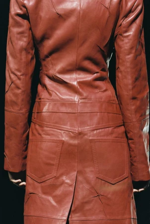 Rear view of a person wearing a red leather patchwork coat against a dark background, showcasing fashion and design details.