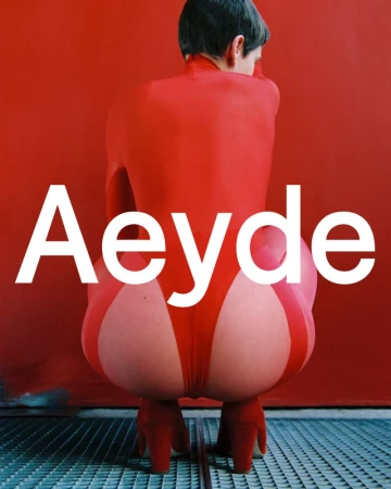 Person in red bodysuit and red shoes, viewed from behind, sits on a blue metal grate against a red background with white logo text.