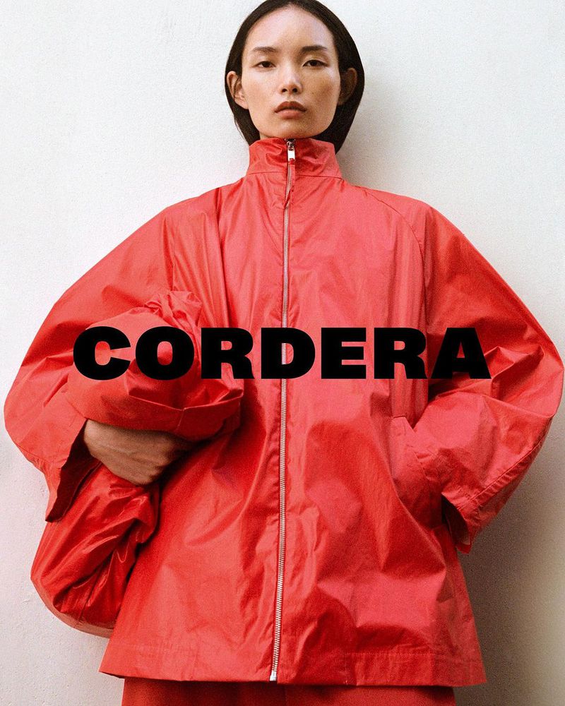 Model wearing a bright red zip-up jacket holding a matching red bag against a plain wall