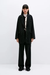 Model standing against a white seamless background wearing a black pinstripe blazer and dark trousers for Cordera.