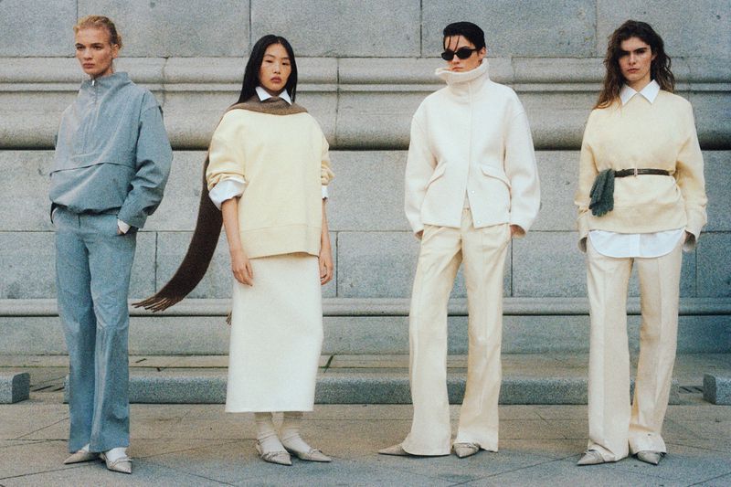Four models in neutral and blue apparel posing outdoors against a pale stone architectural wall for Mango Into The New campaign.