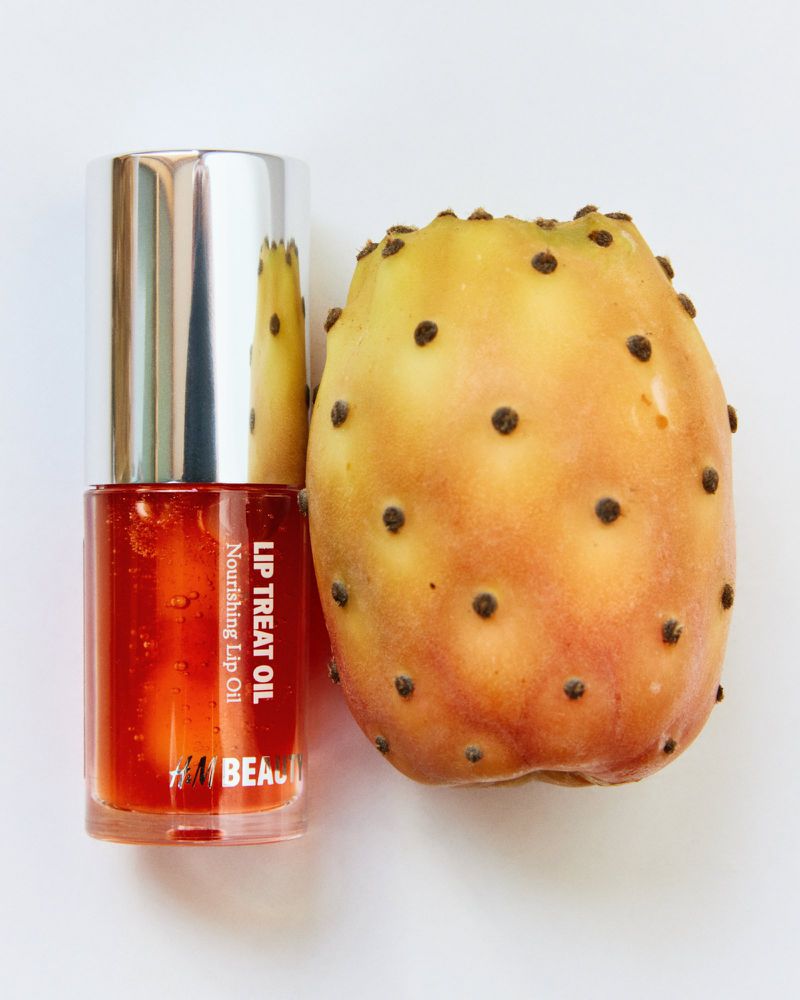 Close-up of H&M Beauty Lip Treat Oil next to prickly pear, highlighting the product's color and texture against the fruit's natural skin.