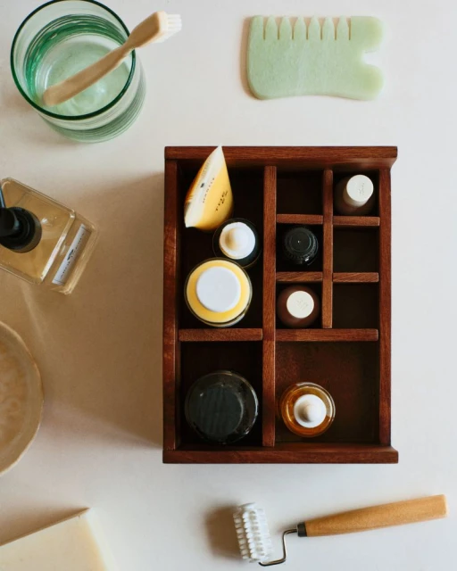 Overhead shot of a wooden cosmetic organizer with various beauty and skincare products on a white surface, alongside a toothbrush and roller.