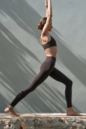 Model Andreea Diaconu posing in a wellness campaign for H&M, practicing yoga outdoors against a textured wall with tree shadows.