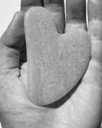 Close-up of a heart-shaped stone gua sha tool resting in the open palm of a hand