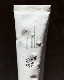 White skincare product tube covered in water droplets against a dark background.