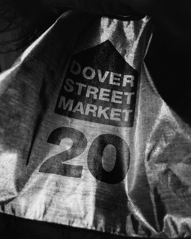 Monochrome image shows a wrinkled textile with the words 'Dover Street Market' and the number '20' printed on it, set against a dark background.