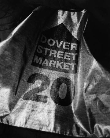Monochrome image shows a wrinkled textile with the words 'Dover Street Market' and the number '20' printed on it, set against a dark background.