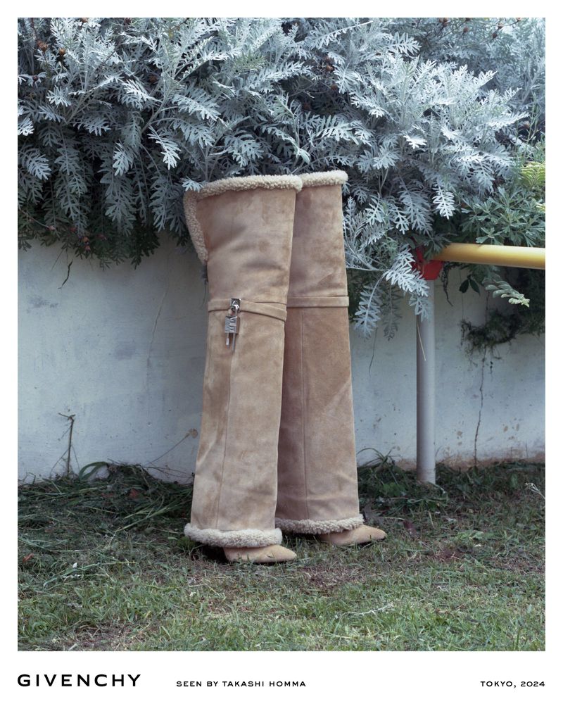 Fashion shot of a pair of high tan suede boots with shearling trim, posed in front of greenery with a concrete wall backdrop.