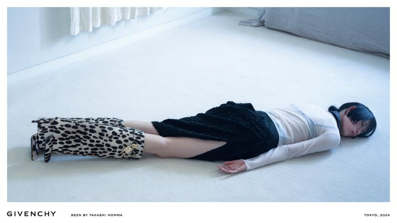 Woman lies on floor wearing black skirt and animal print boots in minimalist setting with a white floor and white walls and window.