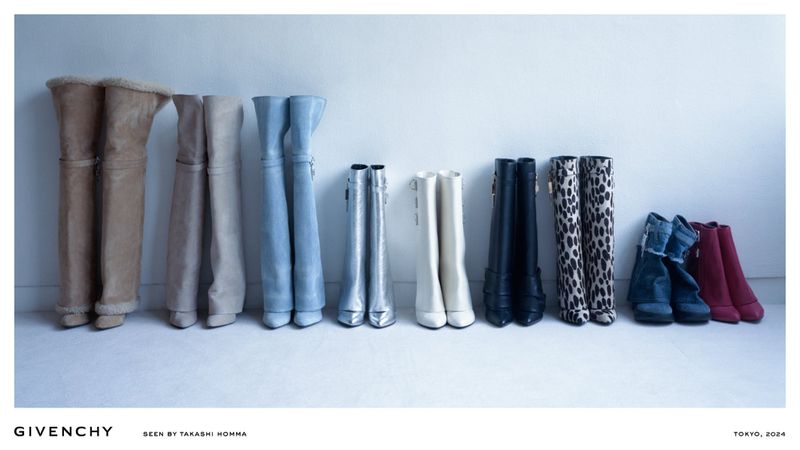 Array of knee-high fashion boots in various colors and materials lined against a white wall in a studio setting for a fashion editorial.
