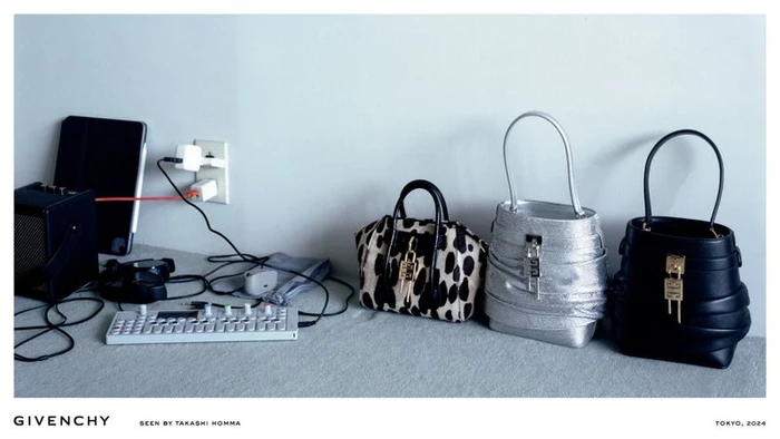Three Givenchy Shark Lock handbags lined up next to electronic audio equipment and tangled cords against a plain wall.