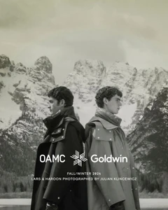 Two young men standing back to back wearing heavy winter coats against a snowy mountain landscape