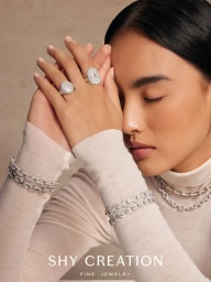 Close-up portrait of a woman wearing diamond rings and chain bracelets against a neutral textured background