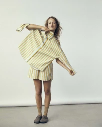 Model in yellow and white striped shirt and matching shorts holding up garment against a white seamless background