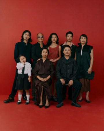 Group portrait of eight people against a vibrant red backdrop, featuring diverse ages and elegant attire, suitable for fashion or family themes.