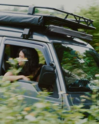 Woman looking out the window of a moving grey SUV driving past lush green foliage captured with motion blur.