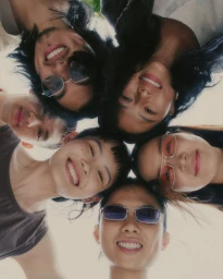 Low angle group portrait of six smiling young adults leaning in together in a tight circle against an open sky