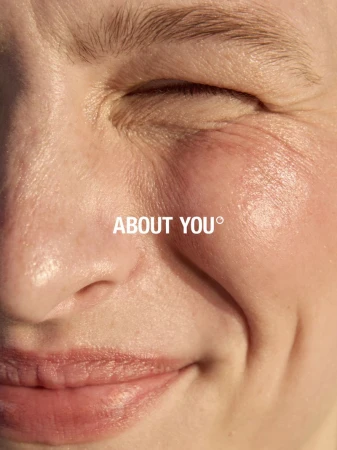 Close-up portrait of a woman smiling with eyes closed under warm natural light for About You FW25