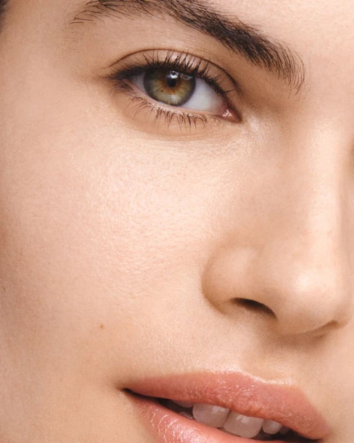 Close-up portrait of an adult female's face showing her eye, skin, and lip makeup in a beauty or fashion context with soft lighting.