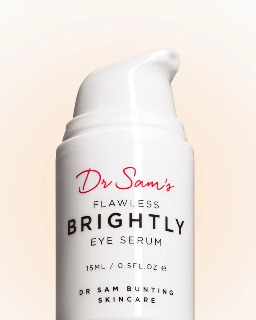 Close-up of a white bottle of Dr. Sam's Flawless Brightly Eye Serum with red and black text on a light peach background.