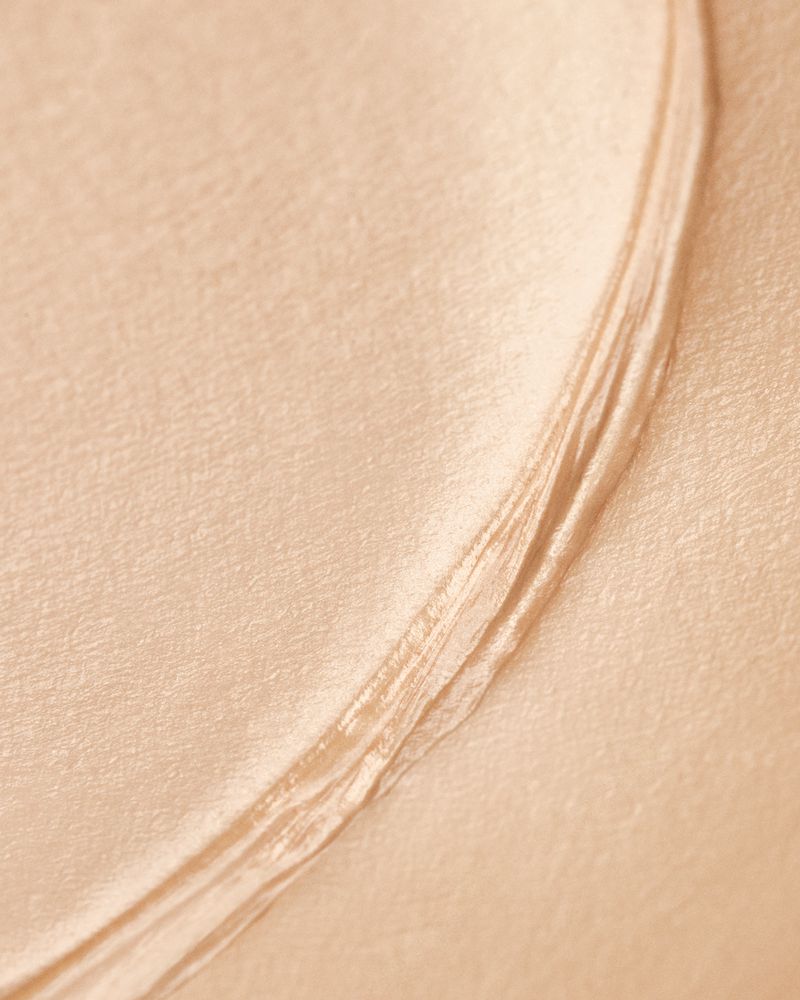 Close-up of light beige fabric with smooth texture and folds, creating soft curves and subtle shadows in a minimalist composition.