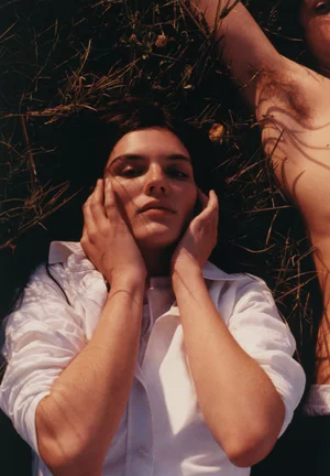 Model Lola Nicon lying in tall grass wearing a white shirt with hands on face for Gimaguas by Lengua
