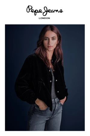 Model in black velvet jacket and grey denim jeans posing against a dark blue background for Pepe Jeans