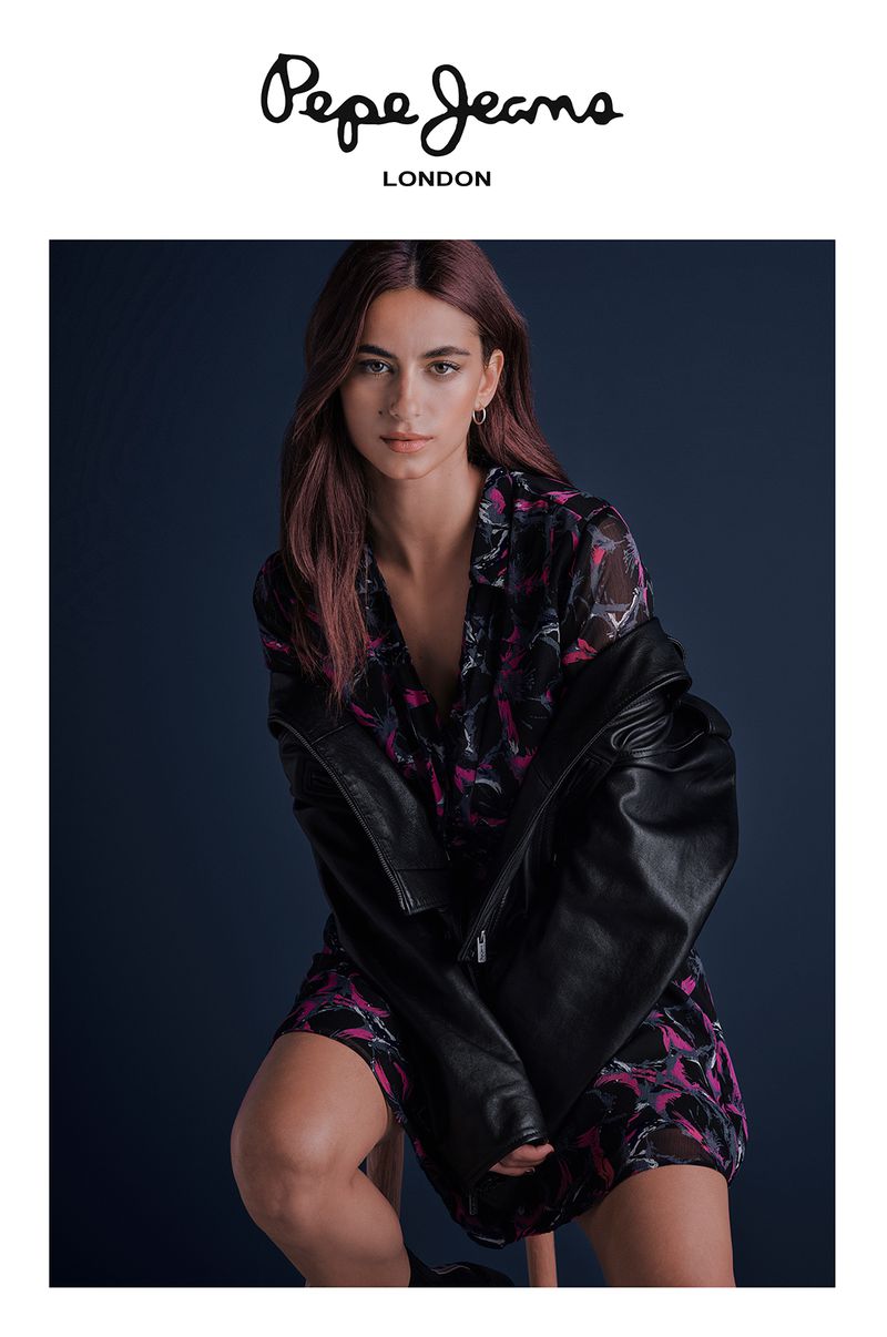 Model in printed dress and leather jacket sitting against dark studio backdrop for Pepe Jeans OI24 campaign.