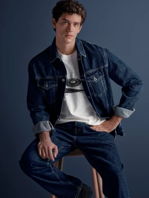 Model Xavier Serrano wearing a denim jacket and jeans, seated against a dark blue studio background for Pepe Jeans OI24.