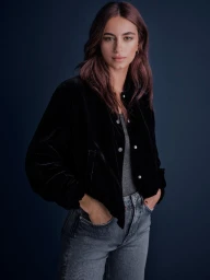 Woman wearing black velvet jacket and grey jeans against a dark blue background for Pepe Jeans