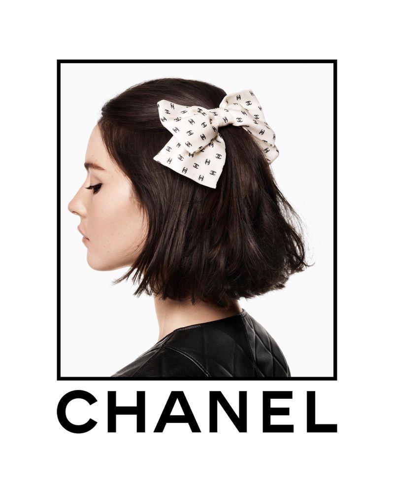 Woman with dark hair in profile wearing a Chanel logo ribbon bow, black quilted jacket, and Chanel logo at the bottom.