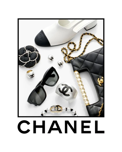 Fashion still life featuring luxury Chanel accessories: handbag, shoe, sunglasses, jewelry, and embellishments on a white background.