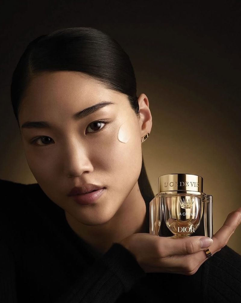 Asian woman poses with Dior beauty product, close-up view, in a beauty shot showcasing skincare with soft lighting and focus on presentation.