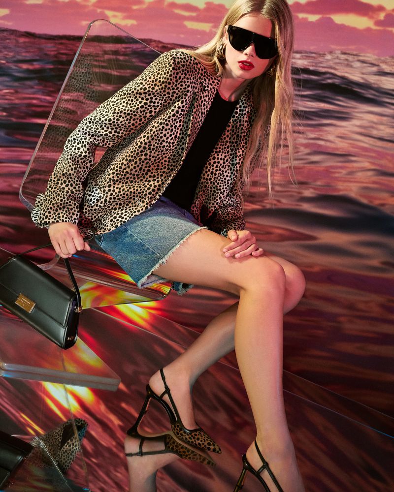 A fair-skinned model with blonde hair and sunglasses poses while wearing a leopard print jacket, mini-skirt, and slingback heels.