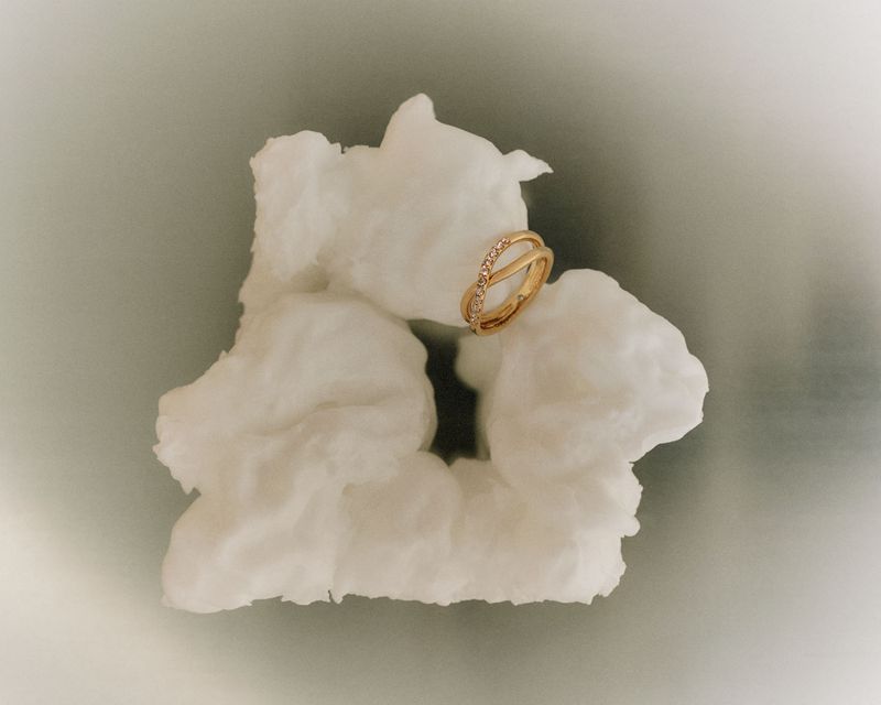 Gold ring with gemstones resting on a textured white surface with a gray background and soft lighting showcasing jewelry design.