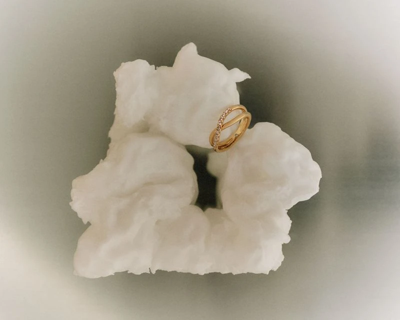 Gold ring with gemstones resting on a textured white surface with a gray background and soft lighting showcasing jewelry design.