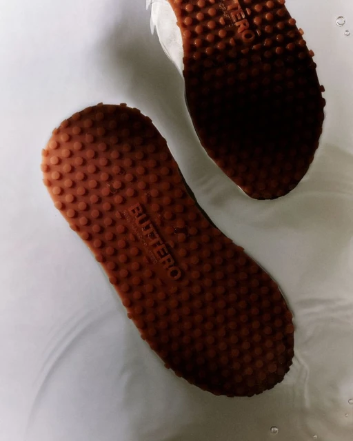 High-angle view of two athletic shoes with textured brown soles and white uppers submerged in water, showcasing the shoe's design and texture.
