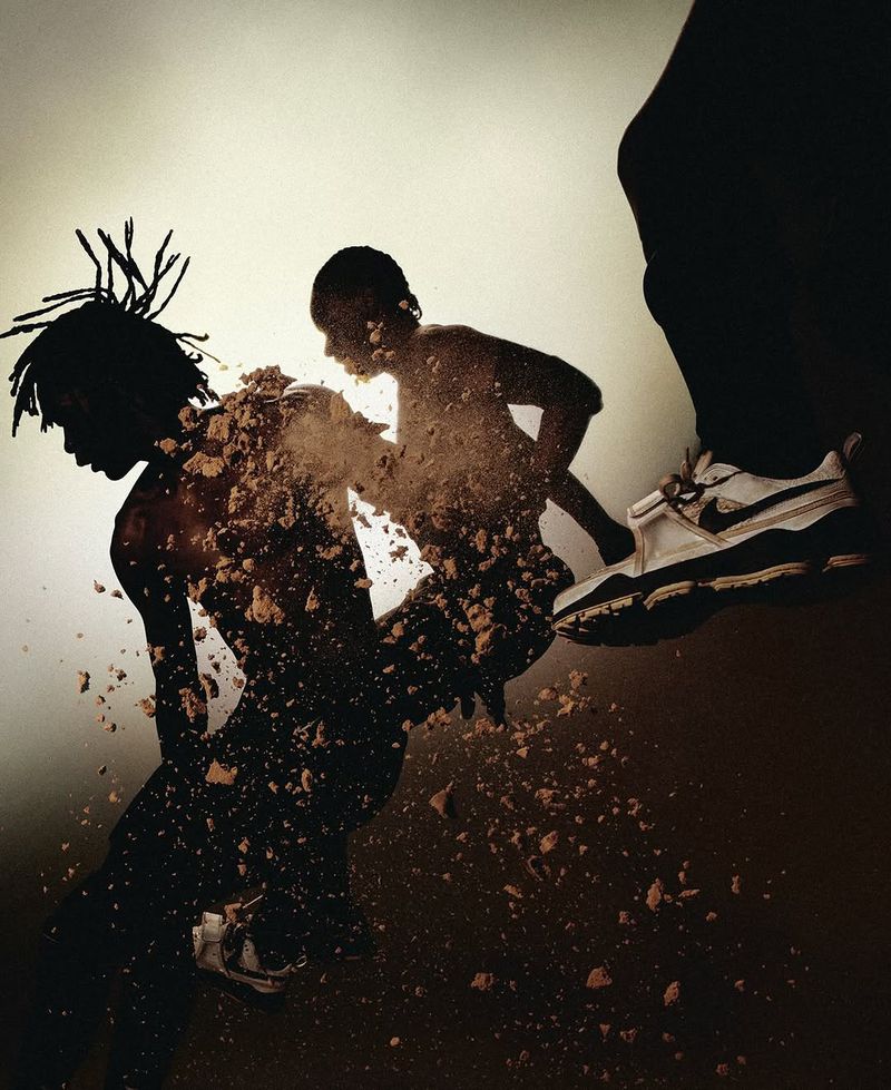 Athletic shot of two people, one with dreadlocks, covered in brown powder with a white sneaker bearing down, studio lighting, high contrast.