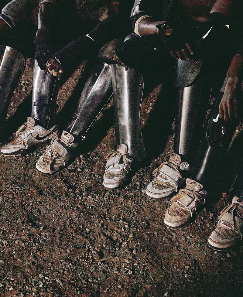 Close-up of a group of people in metal armor wearing athletic shoes standing on dirt. Focus on the shoes, armor and textured ground.