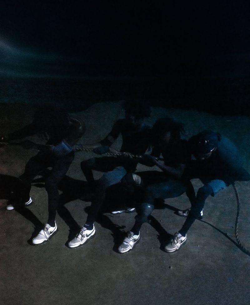 Four adult male athletes engage in a tug-of-war on a dark surface, wearing sports shoes and pulling on a thick rope. Sport.