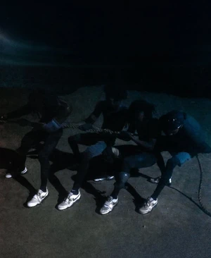 Four figures pulling a heavy rope in low-key lighting wearing athletic sneakers