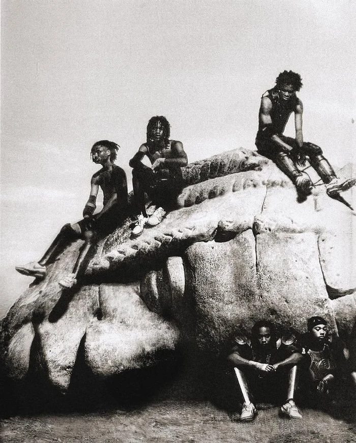 Monochrome editorial image of five Black men posing together on and around a large rock formation for Nike x Travis Scott.