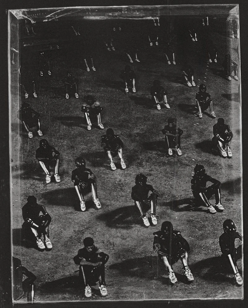 High-angle monochrome shot of multiple seated individuals arranged in a grid-like pattern on a textured ground.