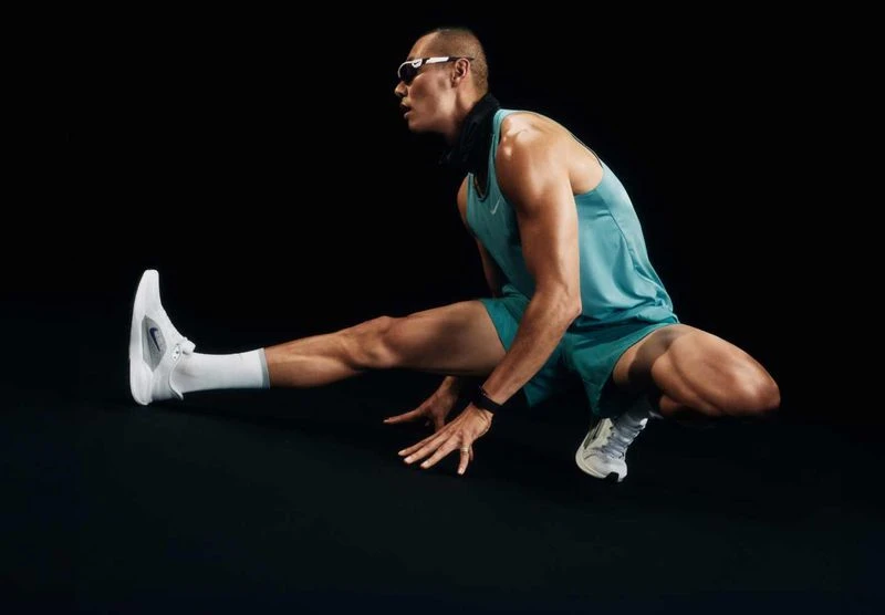 Athletic man in sportswear stretches his legs in front of a black background, showcasing fitness, flexibility, and athletic wear.