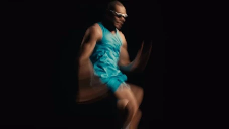 Male runner wearing bright blue athletic wear and white sunglasses in motion against a dark background