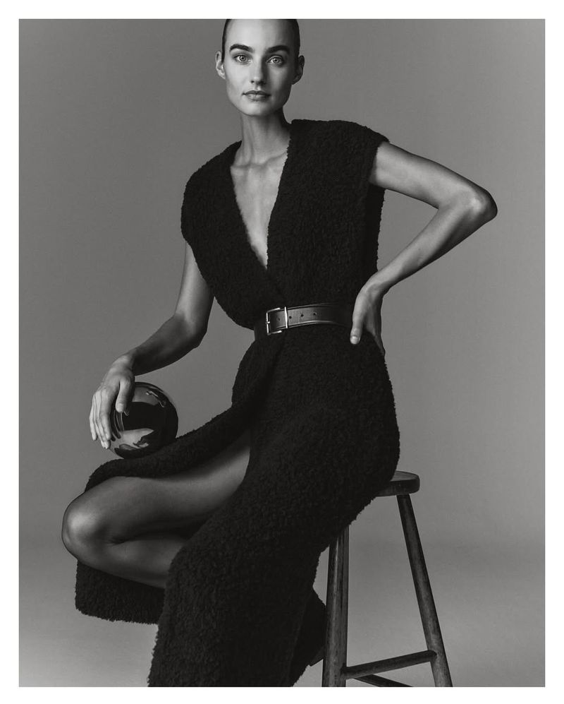 Model Maartje Verhoef seated on a wooden stool wearing a black textured dress for Marc O'Polo