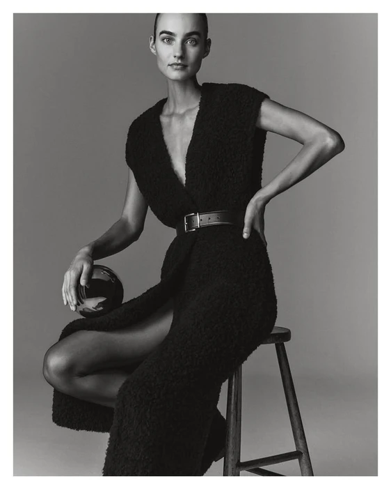Model Maartje Verhoef seated on a wooden stool wearing a black textured dress for Marc O'Polo