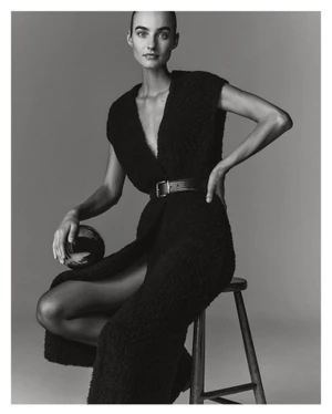 Model Maartje Verhoef seated on a wooden stool wearing a black textured dress for Marc O'Polo